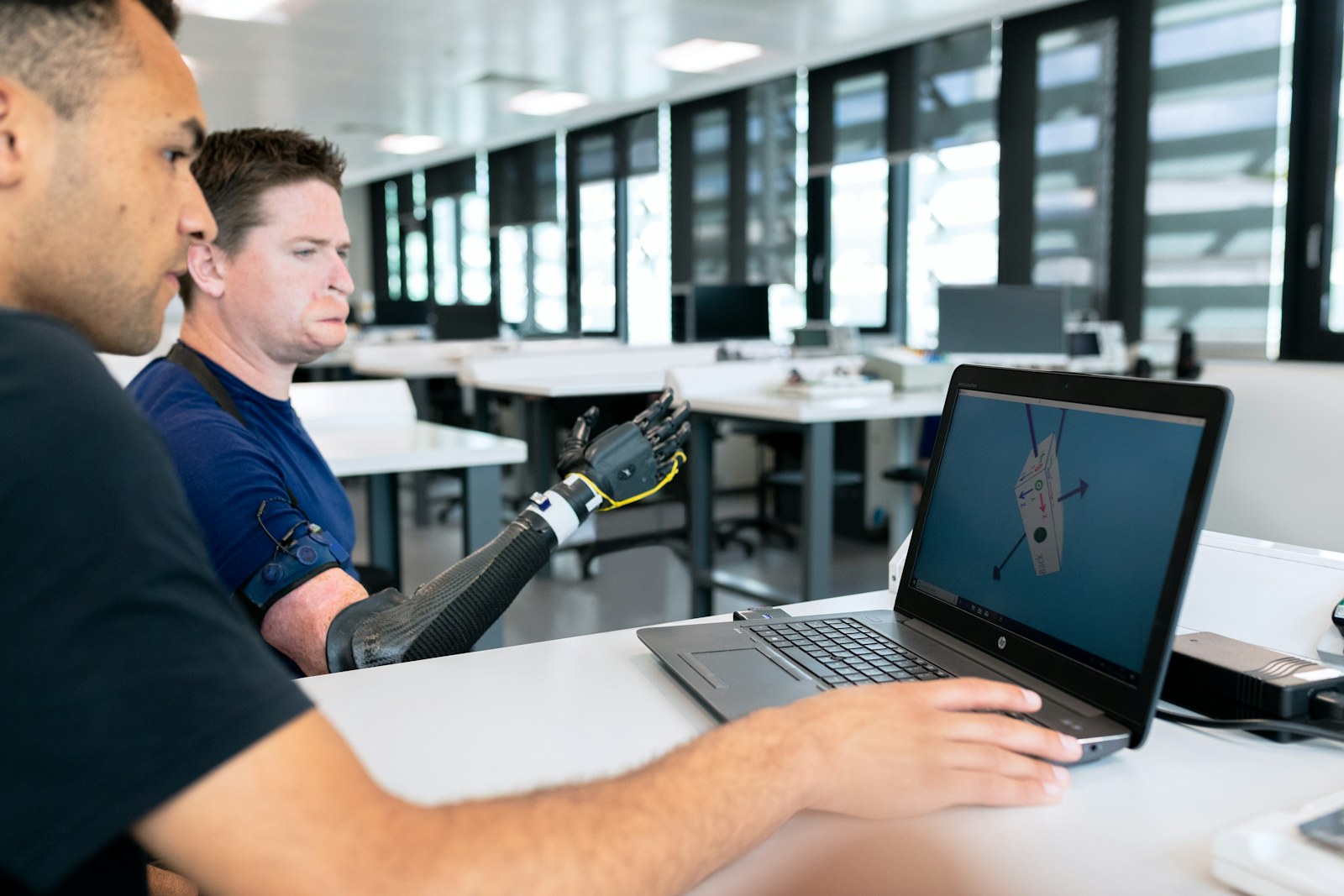 Engineers testing a sensor-enabled prosthetic arm beside a laptop.