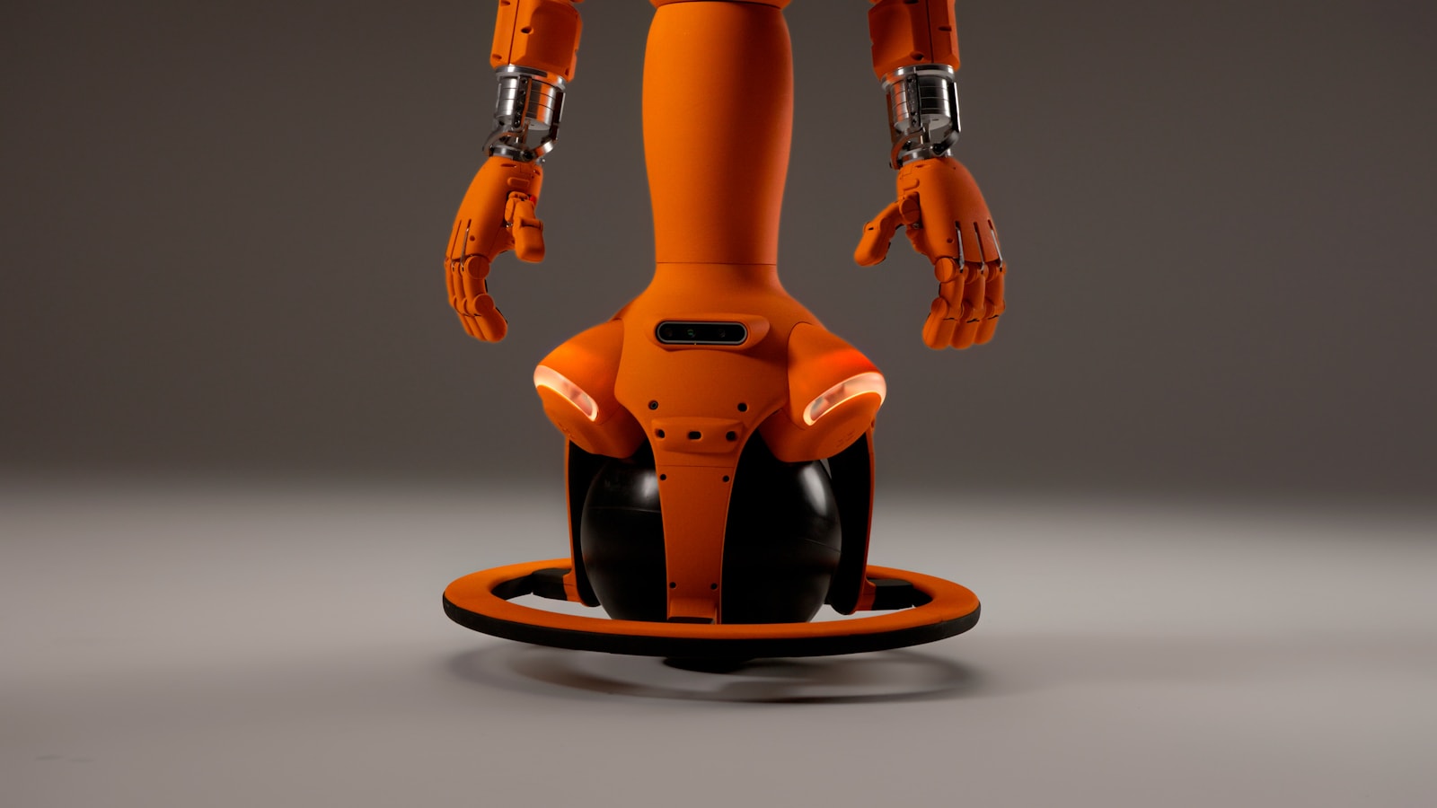 Orange wheeled personal robot with articulated hands in a studio.